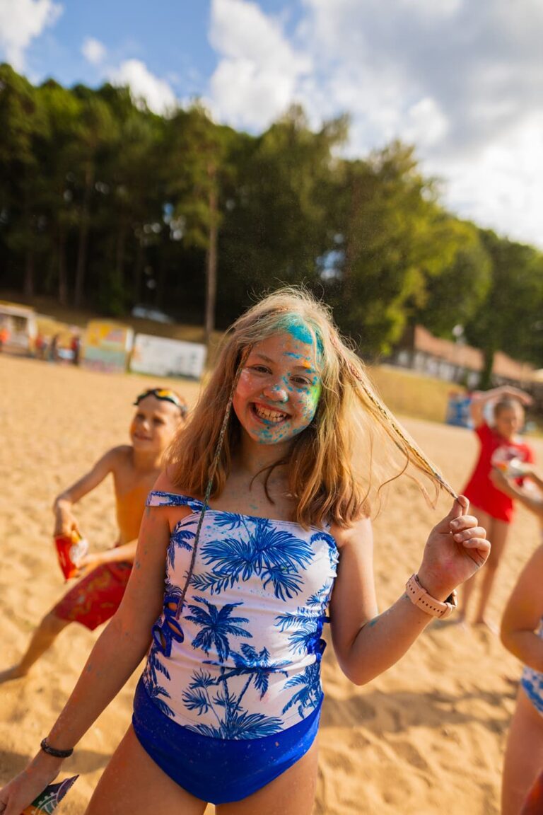 Uśmiechnięta dziewczynka z kolorowym proszkiem na twarzy na plaży. Radosne, wakacyjne chwile.