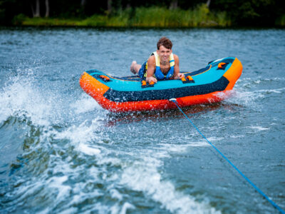 Młody mężczyzna na dmuchanej poduszce wodnej, holowany po jeziorze. Letnia zabawa.