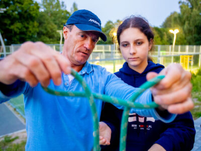 Mężczyzna uczy dziewczynę wiązać węzeł żeglarski. Nauka, przyroda, aktywność.