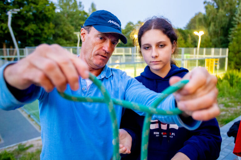 Mężczyzna uczy dziewczynę wiązać węzeł żeglarski. Nauka, przyroda, aktywność.