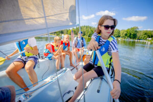 Dzieci na żaglówce uczą się żeglować. Letnia przygoda na wodzie.