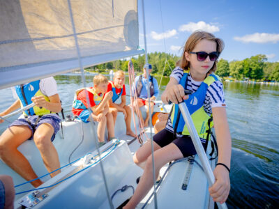 Dzieci na żaglówce uczą się żeglować. Letnia przygoda na wodzie.