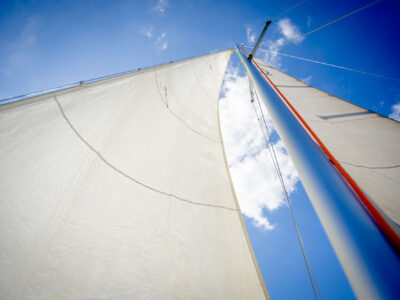 Żagiel na tle błękitnego nieba z chmurami. Żeglarstwo, podróże, wakacje.