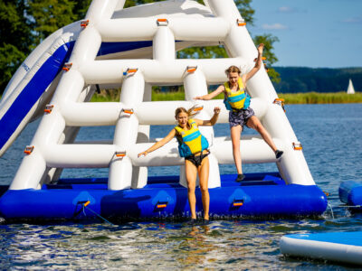 Dwie dziewczyny skaczą z dmuchanej zjeżdżalni wodnej. Letnia zabawa na jeziorze.