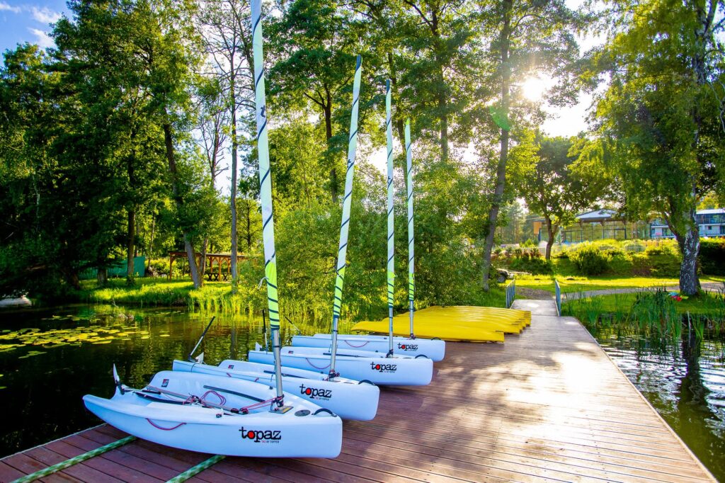 Białe żaglówki Topaz stoją na drewnianym pomoście nad jeziorem. Idealne na wakacje!