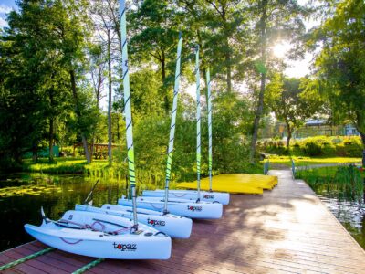 Białe żaglówki Topaz stoją na drewnianym pomoście nad jeziorem. Idealne na wakacje!