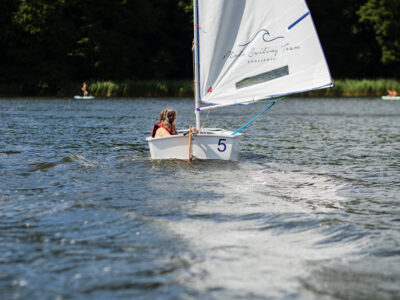 Dziecko na żaglówce uczy się żeglować na jeziorze. Nauka żeglarstwa dla dzieci.