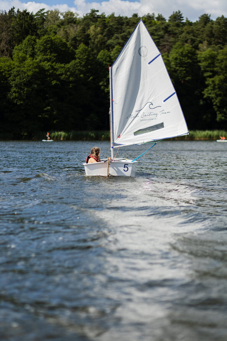 Dziecko na żaglówce uczy się żeglować na jeziorze. Nauka żeglarstwa dla dzieci.