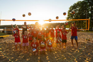 Dzieci i trener bawią się piłkami do siatkówki na plaży w słoneczny dzień.