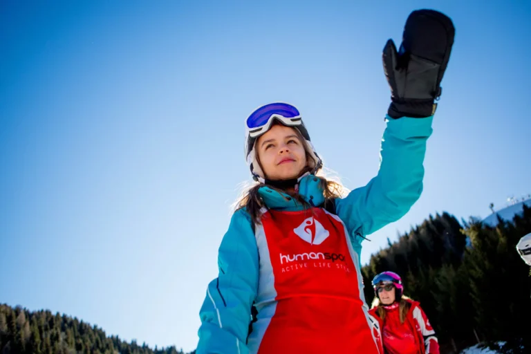 Dziewczynka w stroju narciarskim pozdrawia z góry. Narty, góry, słońce.