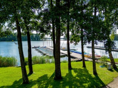 Łódki na jeziorze przy pomoście, otoczone zielenią i drzewami. Wakacje nad wodą.