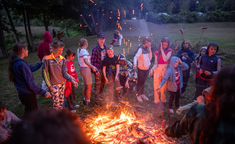 Dzieci pieką kiełbaski nad ogniskiem. Letnia przygoda i wspólne chwile.