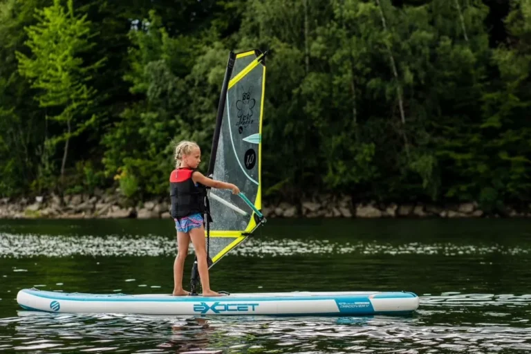Dziewczynka na desce windsurfingowej, nauka żeglowania, aktywność wodna, wakacje na jeziorze.