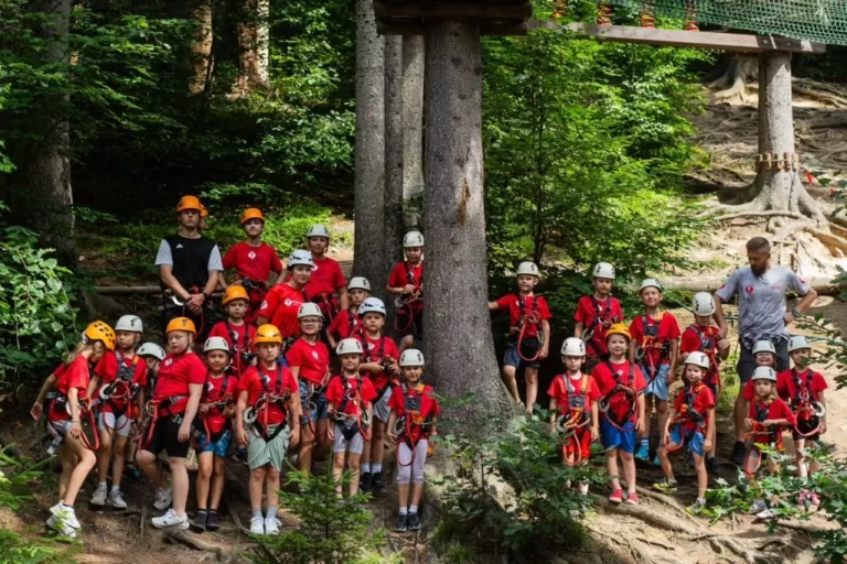Dzieci w kaskach i sprzęcie wspinaczkowym pozują do zdjęcia w lesie. Park linowy.