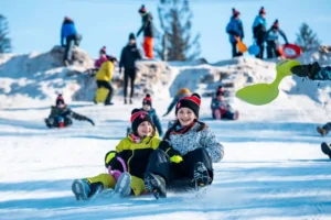 Dzieci zjeżdżają na sankach po ośnieżonym stoku. Radość i zabawa na śniegu.