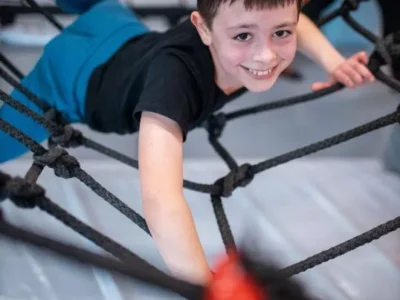 Uśmiechnięty chłopiec wspina się po siatce. Aktywność, zabawa, sport.
