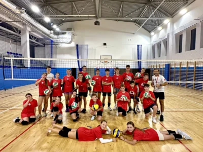 Drużyna siatkarska w czerwonych strojach z piłkami na hali sportowej.