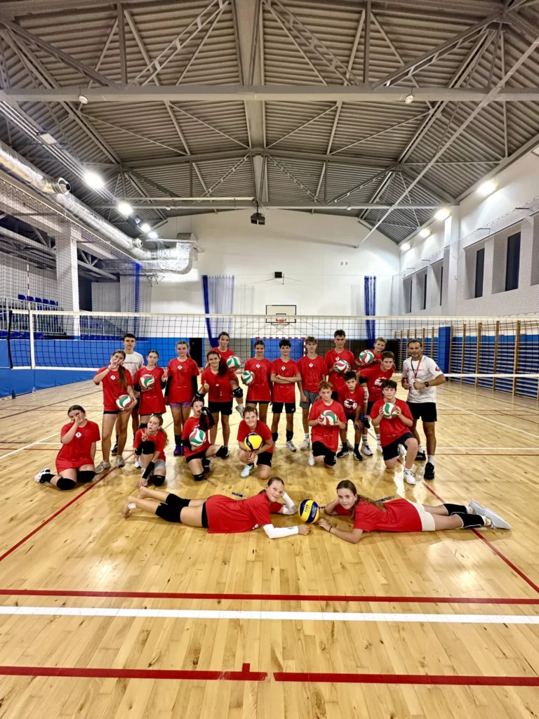 Drużyna siatkarska w czerwonych strojach z piłkami na hali sportowej.