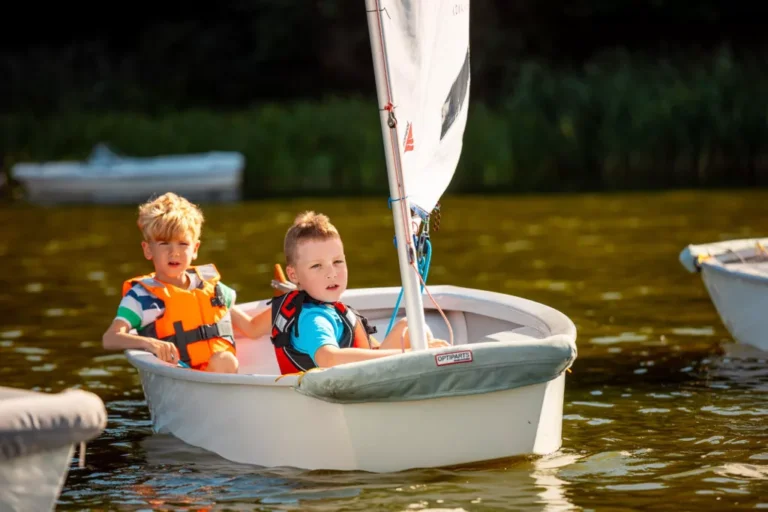 Dzieci na łódce żaglowej, nauka żeglarstwa, wakacje nad wodą, zabawy na jeziorze.