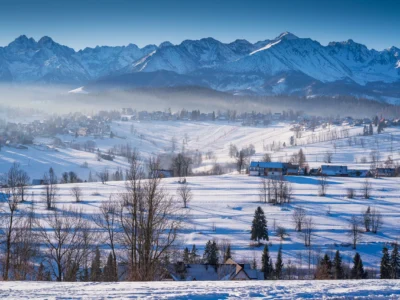 Zimowy krajobraz Tatr: ośnieżone szczyty, mgła i urokliwa wieś.