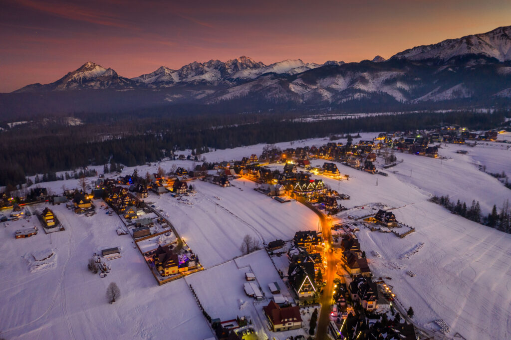 Zimowa wieś w Tatrach o zmierzchu, oświetlone domy i ośnieżone góry.