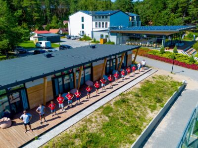 Grupa dzieci w czerwonych koszulkach stoi na tarasie przy nowoczesnym budynku.