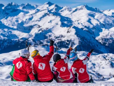 Narciarze w czerwonych kurtkach z logo podziwiają zimowe góry.