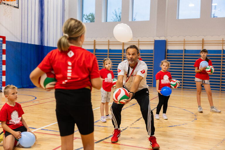 Trener siatkówki z dziećmi na sali gimnastycznej. Nauka gry w siatkówkę.