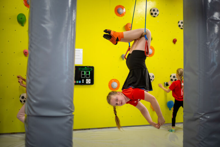 Dziewczynka w zwisie na linie na ściance wspinaczkowej. Zabawa i aktywność fizyczna.