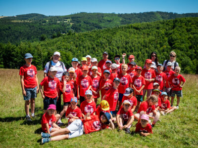 Grupa dzieci w czerwonych koszulkach na tle zielonych wzgórz.