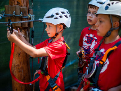 Dzieci w kaskach i szelkach na ściężce linowej. Przygoda i zabawa na wysokości.