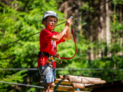 Chłopiec w kasku i czerwonej koszulce na parku linowym, gotowy do zjazdu.