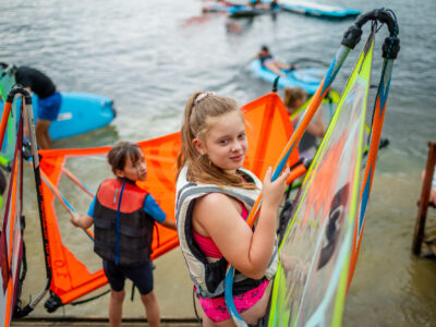 Dzieci przygotowują się do windsurfingu. Wodne sporty dla najmłodszych.
