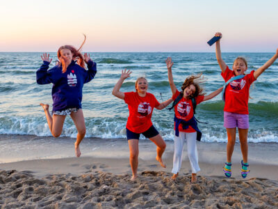 Radosne dzieci skaczą na plaży o zachodzie słońca. Wakacje, morze, szczęście.