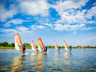 Windsurfing na jeziorze pod błękitnym niebem. Aktywny wypoczynek na wodzie.
