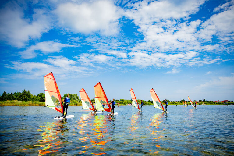 Windsurfing na jeziorze pod błękitnym niebem. Aktywny wypoczynek na wodzie.