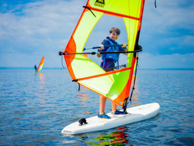 Chłopiec na desce windsurfingowej, słońce, wiatr i woda. Idealny dzień na sport wodny!