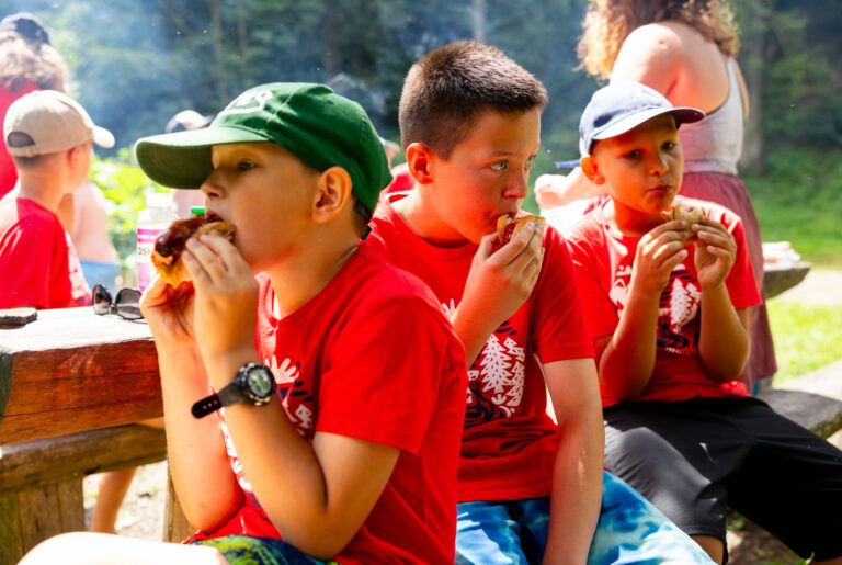 Dzieci jedzą hamburgery na pikniku.