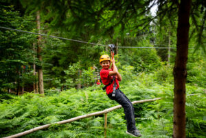 Chłopiec na zjeżdżalni tyrolskiej w lesie. Przygoda i zabawa na świeżym powietrzu.
