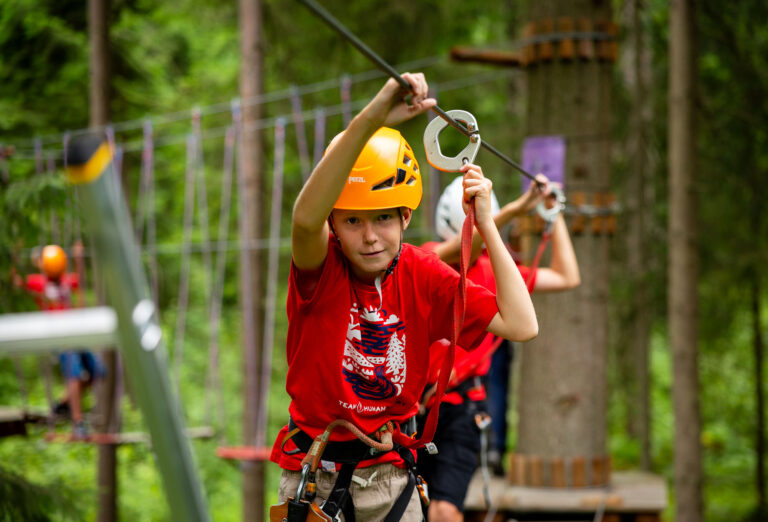 Chłopiec w kasku na parku linowym, pokonuje trasę zjazdową.