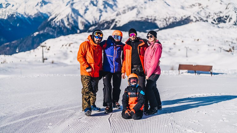 Grupa narciarzy pozuje do zdjęcia na tle ośnieżonych gór.