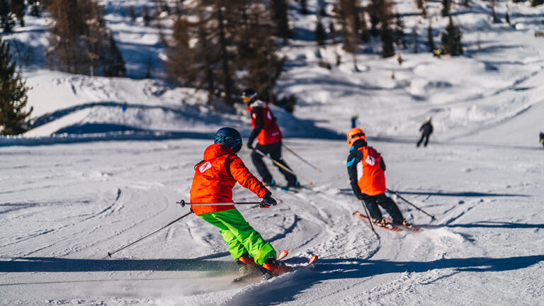 Dzieci na nartach zjeżdżają po ośnieżonym stoku w słoneczny dzień.
