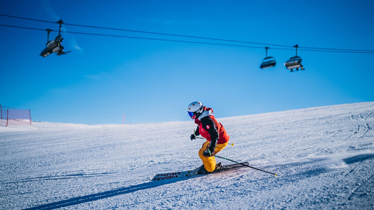 Narciarz zjeżdża po stoku. W tle widać kolej linową.