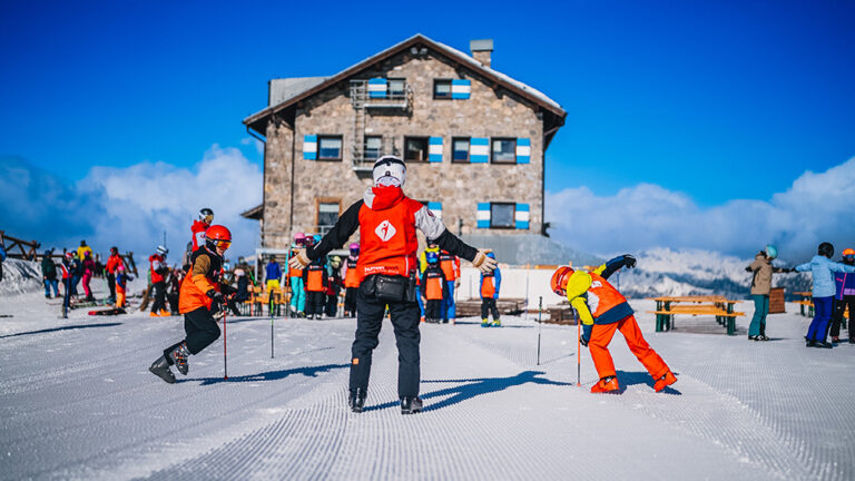 Nauka jazdy na nartach z instruktorem. Dzieci w kolorowych strojach na stoku.