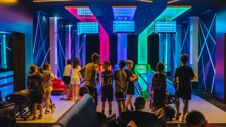 Dzieci bawiące się w kręgielni z kolorowym oświetleniem.