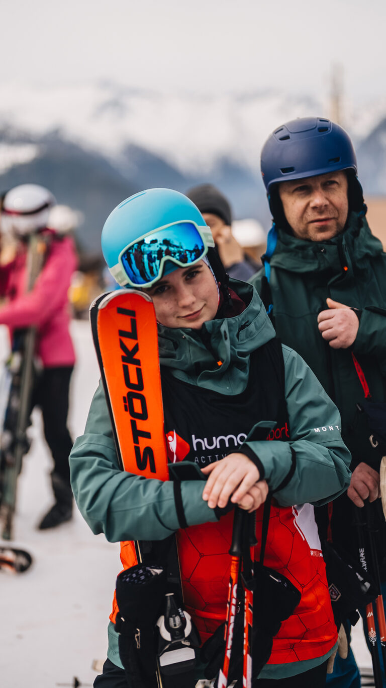Młoda narciarka w niebieskim kasku i goglach, trzymająca narty Stöckli.