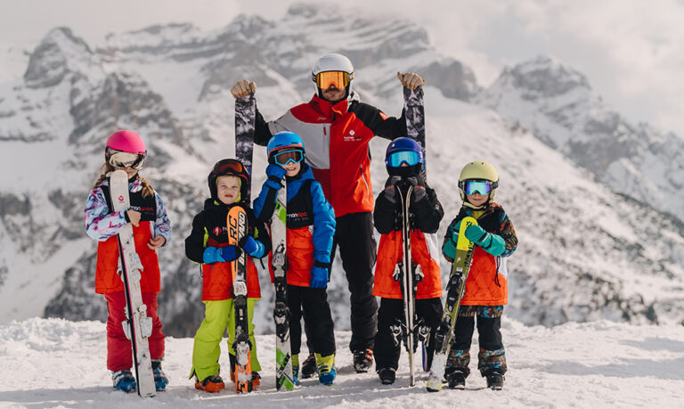 Grupa narciarzy, w tym dzieci i instruktor, pozuje na tle gór.