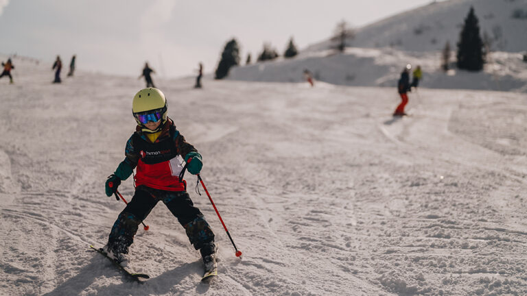 Dziecko na nartach w kasku i goglach, z kijkami, na ośnieżonym stoku.