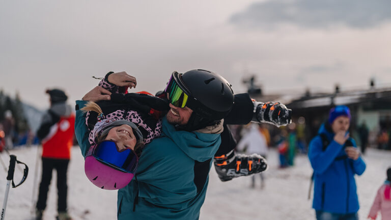 Ojciec niesie córkę na nartach. Radość i zabawa na stoku.