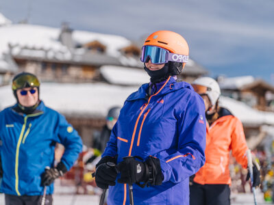 Narciarze w kolorowych kurtkach i kaskach na stoku narciarskim.